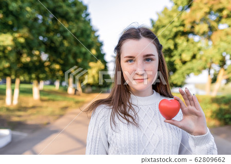 Teen girl 12-13-14 years old, summer park, holding red toy heart her hands. Free space copy text. Concept donation, helping children, mother's day, care support for adolescents. St. Valentine's Day. Teen girl 12-13-14 years old, summer park, holding red toy heart her hands. Free space copy text. Concept donation, helping children, mother's day, care support for adolescents. St. Valentine's Day. 62809662