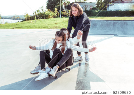 3 girls schoolgirls ride skateboard, rest after school institute college weekend. Summer city, sports ground. Emotions happiness, fun, joy, laughter, smile, entertainment. Casual wear sweater jeans. 3 girls schoolgirls ride skateboard, rest after school institute college weekend. Summer city, sports ground. Emotions happiness, fun, joy, laughter, smile, entertainment. Casual wear sweater jeans. 62809680