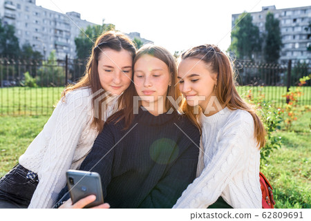 3 teenage girls recording video photograph on phone. In summer city. Emotions happiness, joy, fun, smile. Selfie photo. Portrait a smartphone. Social networks video clip Internet. Online application. 62809691