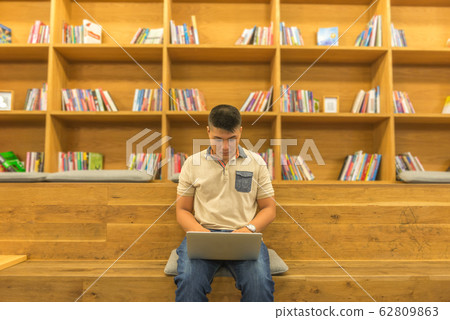 Asian student using laptop at wooden library bookshelf background Asian student using laptop at wooden library bookshelf background 62809863