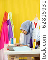 A young beautiful Asian Muslim woman designer who wore a hijab as a startup business owner is considering the fabric to be sewn. 62815931