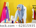 A young beautiful Asian Muslim woman designer who wore a hijab as a startup business owner standing in her working studio room with colorful cloth, dress, thread and sewing machine. 62815935