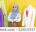 A young beautiful Asian Muslim woman designer who wore a hijab as a startup business owner standing beside her cloth pattern model in her tailor shop. 62815937