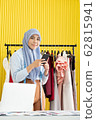A young beautiful Asian Muslim woman designer who wore a hijab as a startup business owner is smiling and holding a mobile phone on her hand in her working studio. 62815941