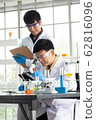 Science, Chemistry, Technology, Biology and Laboratory concept - Asian Senior scientist looks into something on a petri dish while Asian junior scientist taking notes. 62816096