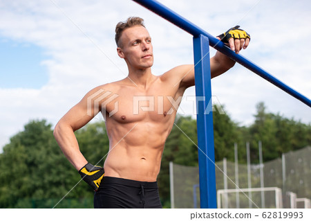 A muscular man stands near parallel bars, with a A muscular man stands near parallel bars, with a 62819993