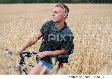 A man in a field on a bicycle. Against the 62819999