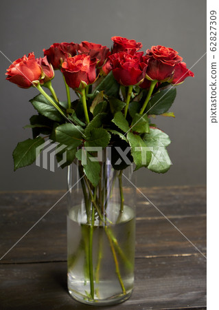Bouquet of red-orange roses in a glass vase on a 62827309