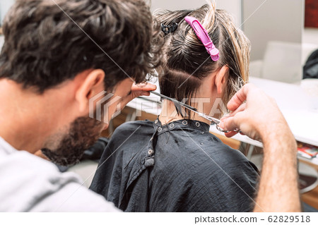 Master hairdresser cuts hair of blond woman in salon. Close up photo 62829518