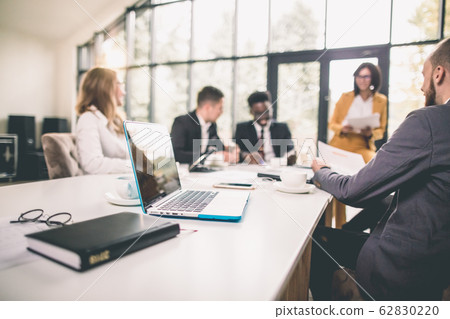 Successful team leader and business owner leading informal in-house business meeting. Businessman working on laptop in foreground. Business and entrepreneurship concept. 62830220