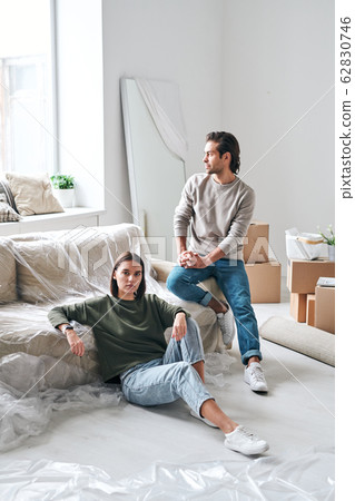 Young tired woman and her husband in casualwear having rest by couch by window Young tired woman and her husband in casualwear having rest by couch by window 62830746