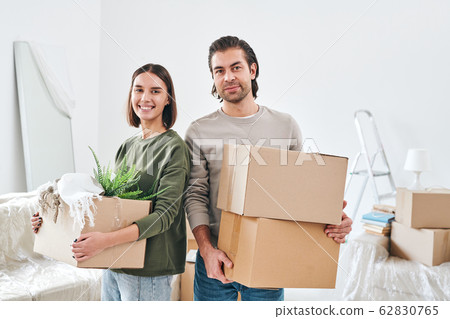 Young smiling woman and her husband with packed boxes looking at you Young smiling woman and her husband with packed boxes looking at you 62830765