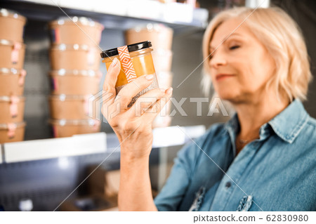 Smiling mature woman reading information on products in store Smiling mature woman reading information on products in store 62830980
