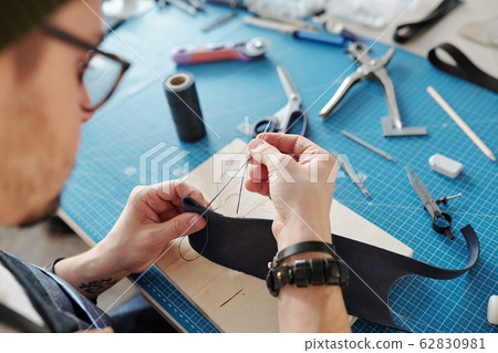 Contemporary craftsman sewing two parts of black leather together Contemporary craftsman sewing two parts of black leather together 62830981