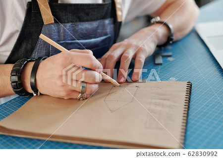 Hand of young craftsman with pencil over page of notepad while drawing sketch 62830992