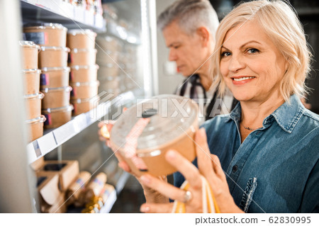 Happy adult woman holding food box in hands in shop 62830995