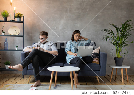 A young Couple on the Couch are Passionate about Gadgets. Small Children Play Around Their Parents. Social Photo. A young Couple on the Couch are Passionate about Gadgets. Small Children Play Around Their Parents. Social Photo. 62832454