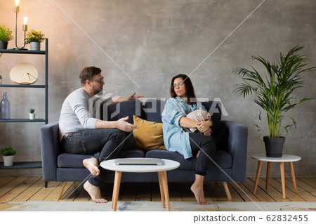 Young Couple Arguing on the Couch at Home. The Husband Shouts at him Wife. Social Photo. Aggression, Suppression. Young Couple Arguing on the Couch at Home. The Husband Shouts at him Wife. Social Photo. Aggression, Suppression. 62832455