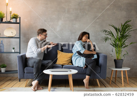 Young Couple Arguing on the Couch at Home. The Husband Shouts at him Wife. Social Photo. Aggression, Suppression. 62832459