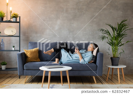 Young woman with Glasses is Lying on the Couch and Texting on the Phone. Young woman with Glasses is Lying on the Couch and Texting on the Phone. 62832467