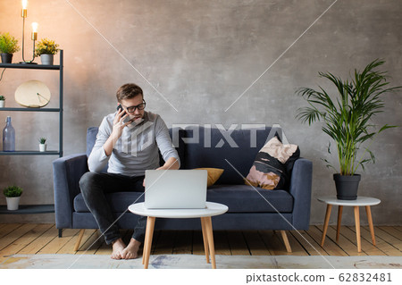 Young man in glasses angry talking on the phone sitting on the couch. Young businessman. Young man in glasses angry talking on the phone sitting on the couch. Young businessman. 62832481