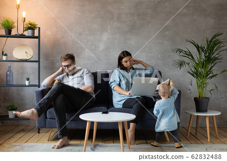 A young Couple on the Couch are Passionate about Gadgets. Small Children Play Around Their Parents. Social Photo. A young Couple on the Couch are Passionate about Gadgets. Small Children Play Around Their Parents. Social Photo. 62832488