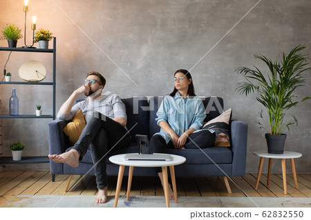 Young Couple Sitting on the Sofa. The Woman Tears Up The Photo. Family Conflict. Young Couple Sitting on the Sofa. The Woman Tears Up The Photo. Family Conflict. 62832550
