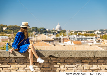 Female watching Rome from the panoramic balcony in the Orange Garden. Woman in blue dress and white straw hat 62833515