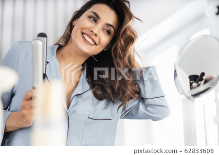 Happy pretty woman holding curling iron at home 62833608