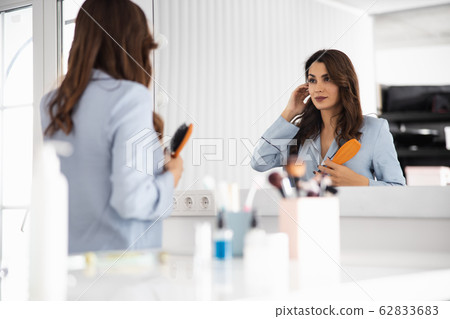 Pretty young woman combing her hair at home Pretty young woman combing her hair at home 62833683