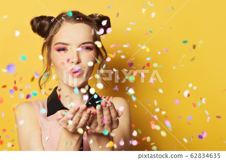 Happy cheerful girl blowing confetti on colorful Happy cheerful girl blowing confetti on colorful 62834635