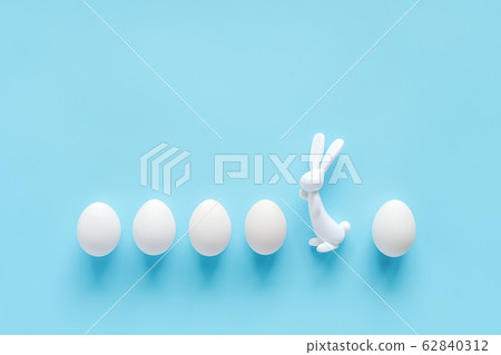 Row white eggs and bunny rabbit figurine on blue Row white eggs and bunny rabbit figurine on blue 62840312
