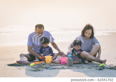 Family playing on the beach. Parents and children relaxing on the beach in the summer.happy healthy family Grandfather and Nephew building sand castle on the beach smiling and carefree. 62841702