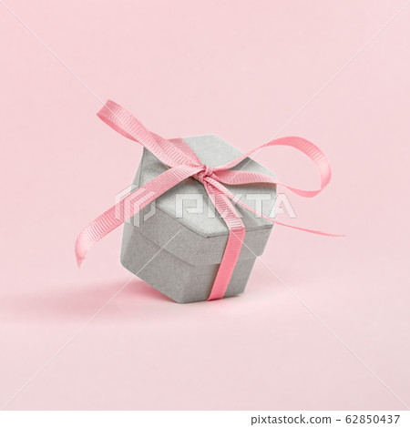 Gift box of irregular shape tied with a pink ribbon on a pink background. 62850437