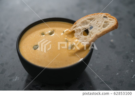 Pumpkin cream soup with pumpkin seeds and baguette crouton in a black bowl on concrete background 62853100