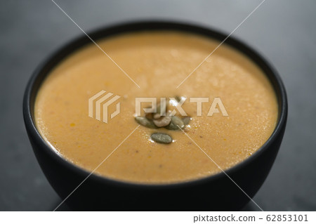 Pumpkin cream soup with pumpkin seeds in a black bowl on concrete background 62853101