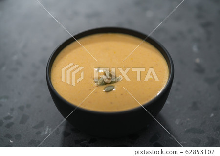 Pumpkin cream soup with pumpkin seeds in a black bowl on concrete background 62853102
