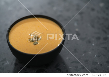 Pumpkin cream soup with pumpkin seeds in a black bowl on concrete background Pumpkin cream soup with pumpkin seeds in a black bowl on concrete background 62853103