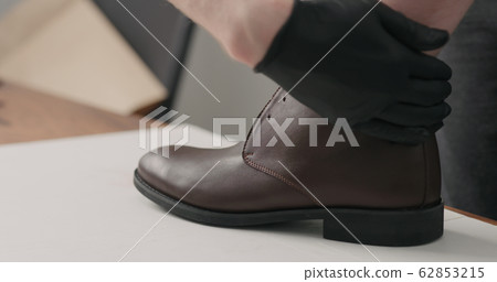 man hands in black gloves applying protective cream to brown leather chukka boots 62853215