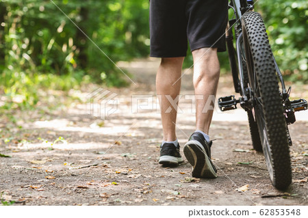 Legs of male cyclist leading bike down the forest trail 62853548