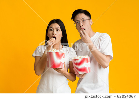 Shocked asian guy and girl eating popcorn, watching movie Shocked asian guy and girl eating popcorn, watching movie 62854067