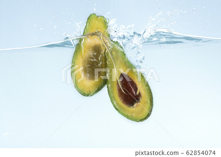 Tasty avocado cut in half dropping into transparent water on blue background Tasty avocado cut in half dropping into transparent water on blue background 62854074