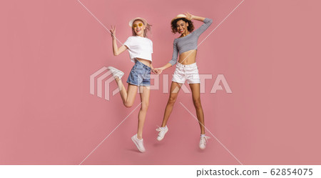 Two attractive young girls in summer clothes jumping on pink background, panorama Two attractive young girls in summer clothes jumping on pink background, panorama 62854075