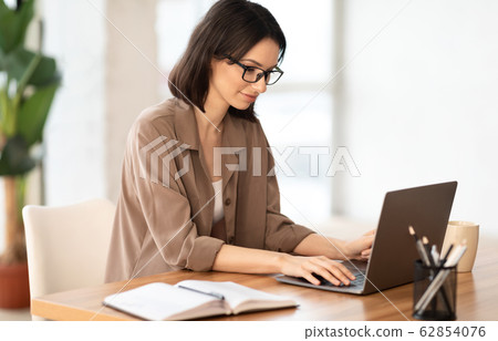 Beautiful girl working on her laptop at contemporary office Beautiful girl working on her laptop at contemporary office 62854076