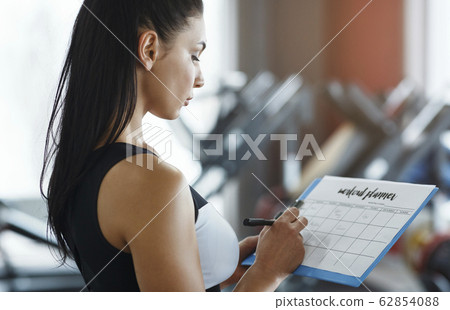 Personal trainer with clipboard making workout plan in gym 62854088