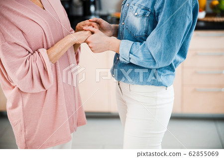 Grandmother and adult granddaughter holding hands at home 62855069