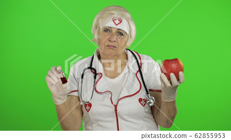 Portrait of elderly caucasian female doctor chooses treats medications or fruits 62855953
