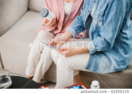 Young lady using digital tablet while sitting on couch with old woman 62856129