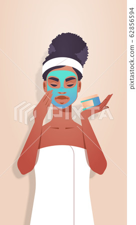 young woman applying clay face mask dressed in towel african american girl skincare spa facial treatment concept portrait vertical 62856594