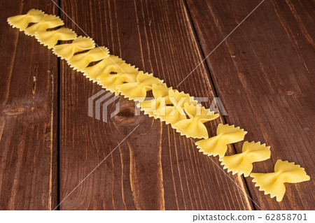 Yellow farfalle pasta on brown wood Yellow farfalle pasta on brown wood 62858701